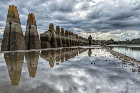 Emma Thorley-Cripps Stone pillars on the left of the picture are reflected onto pools of water left on the causeway from the tide having receded. 
