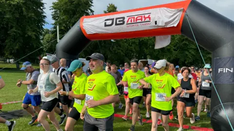 Various runners setting off from an inflatable start line, some wearing bright green tops