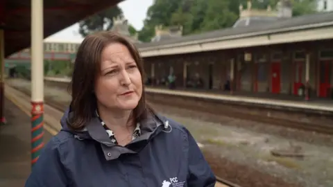 Close up of Police and Crime Commissioner for Devon, Cornwall and Isles of Scilly Alison Hernandez. She is standing on the platform of a train station. She is wearing navy blue waterproof jacket.