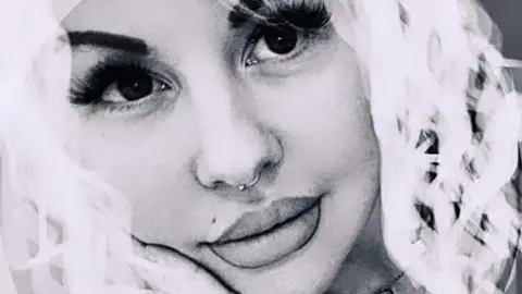 A black and white photo of Jade Duncan. She has large dark eyes, a ring in her nose and thick white curly hair.