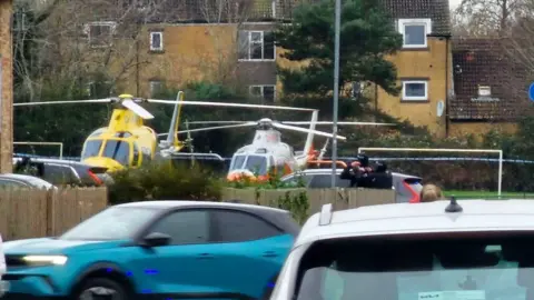 Two helicopters on the ground in an urban park.