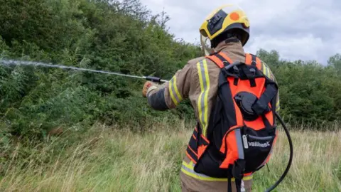 Northamptonshire Fire and Rescue A firefighter with a backpack spraying a jet of water into a field