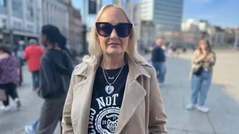 Zoe Cooke - a woman with blonde hair and wearing sunglasses stood outside. 