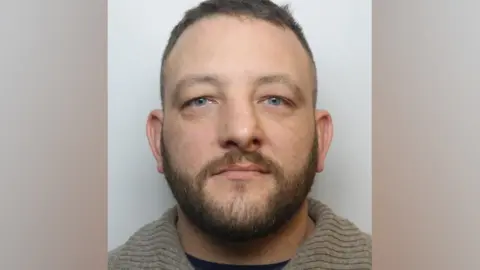 Wiltshire Police Police custody image of Scott David - he has facial hair and is wearing a grey top