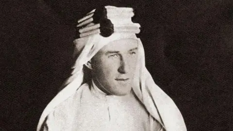 A black and white photo of Col T.E.Lawrence wearing a white Arab robe and headdress.