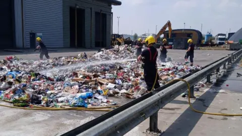 Fenland District Council Firefighters dampen down piles of smouldering waste.