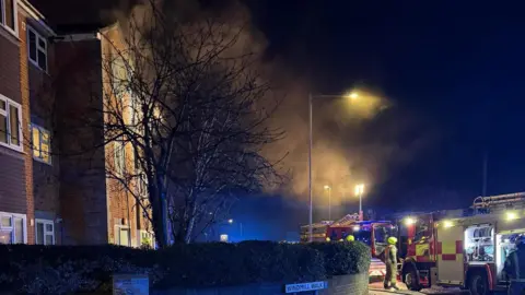Smoke in the air, coming from a block of flats, with fire engines on the scene
