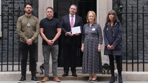 PA Media Five people - three men and two women - standing outside 10 Downing Street. Sir Liam Fox is in the centre of the image and is holding a letter. 