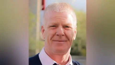 A Facebook picture of Colin Scott looking straight at the camera. He has short, white hair and is smiling