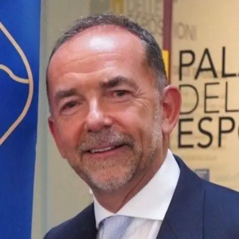 Ronnie Convery A man with receding dark hair and salt and pepper stubble looks into the camera. He is wearing a blue suit with a white shirt and light blue tie