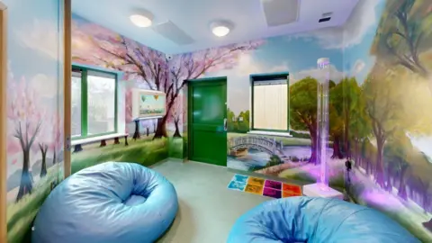 A room with murals of trees with pink blossoms, big blue beanbags and a pink lava lamp.