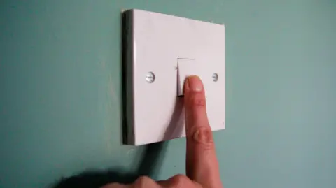 Finger on white lightswitch against green wall 