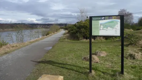 Ryton Willows. A map of the nature reserve stands to the right of the picture. The Keelman's Way path runs along the edge of the river to the left.