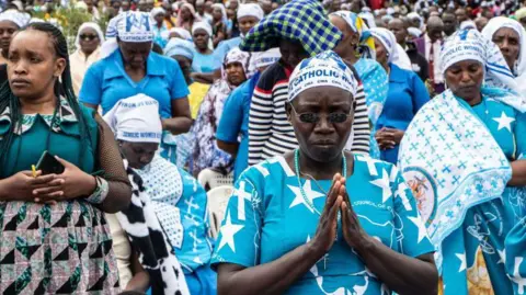 Getty Images Women with heads bowed and hands held in prayer during an outside mass at the Subukia National Shrine in Kenya - October 2024