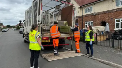 Council works lift bulky waste onto the bag of a truck after carrying out a collection at a property