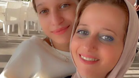 Family Handout Dania Alafranji is with her mother Hayat Ghalayini, both are smiling. Dania is wearing a white top and a necklace. Hayat is wearing a cream headscarf. 