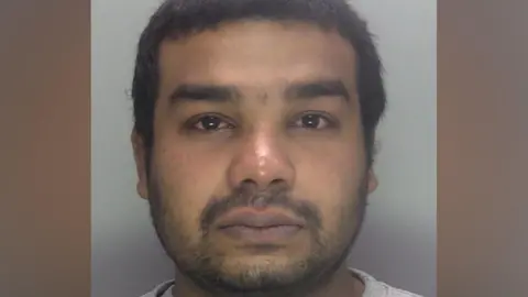 A custody image shows a close-up of Suleman Mukaish facing the camera with a plain light background behind him.