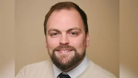 Rosetta Primary School A bearded man with a cream jumper white shirt and blue tie