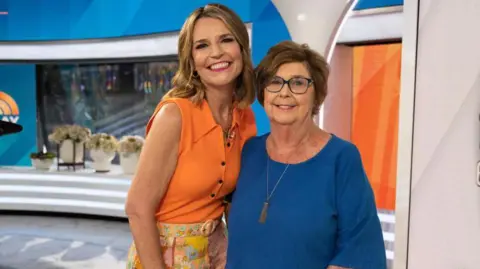 Savannah Guthrie and her mother Nancy smiling with their arms around each other in a TV news studio