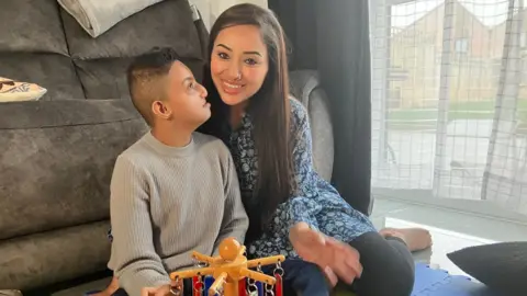 An adult sitting on the floor with a child beside a sofa, with a toy in front of them in a living room.