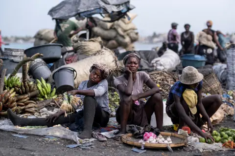 Ricardo Arduengo / Reuters People with fresh produce sit at a market in Cap-Haitien, Haiti, on 21 July 2021