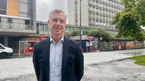 Cabinet member for finance and city centre champion Mark Lowry in a blue shirt and blue check blazer at the front of the Civic Centre in Plymouth
