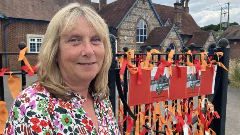 BBC Anna Way in a colourful dress stood at the gates of the school building