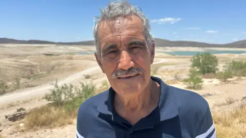 Volunteer water monitor Rafael Betance looks at the camera, standing in front of very parched-looking countryside