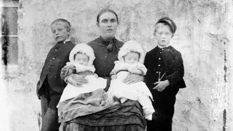 Shetland Museum & Archives A young mother with four children - two young boys in black standing beside her and two girls sitting on her lap dressed in white. 