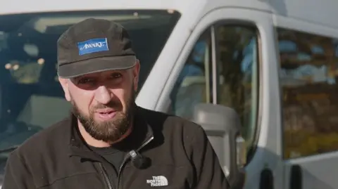Supplied A head and shoulders image of Jake Trask. He is wearing a black North Face jacket over a black T-Shirt and a black cap. He is looking directly into the camera and standing in front of a van.