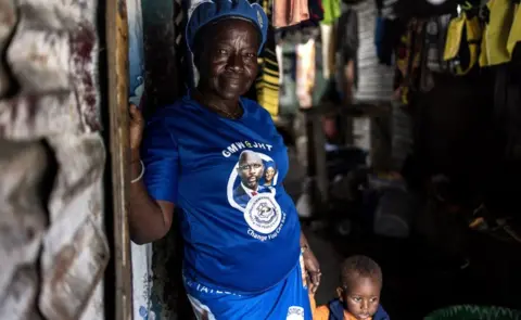 John Wessels/AFP Cathrine poses for a picture with a t-shirt of the President of Liberia George Weah on it in Clara town, Monrovia on October 4, 2023.