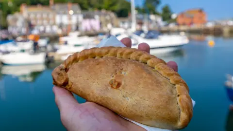 A Cornish pasty in someone's hand, Harbour of Padstow in the background