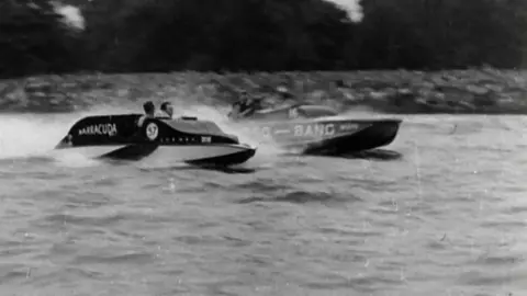 Black and white image of two speedboats racing along Oulton Broad