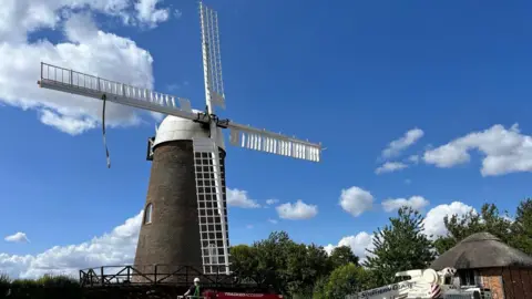 Peter Wilson A windmill with four white sails set against a blue and slightly cloudy sky.
