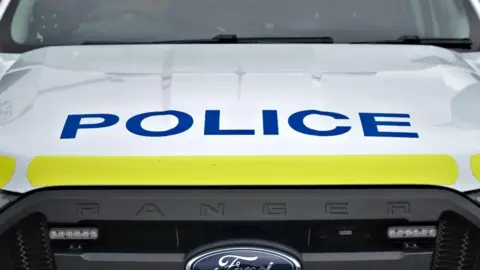 The bonnet of a police van, a white ford ranger vehicle with a strip of yellow on the front of the bonnet and POLICE in nay blue on the bonnet.