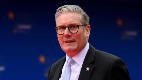 Getty Images British Prime Minister Keir Starmer stands against a royal blue back drop wearing a dark blazer.