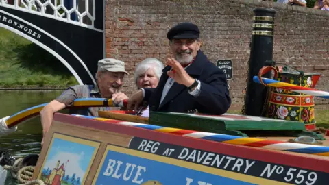 Braunston Marina Sir David Suchet with a black cap waving from a narrowboat