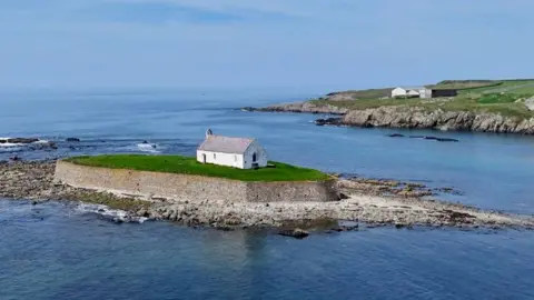 A small white church is seen standing on an island