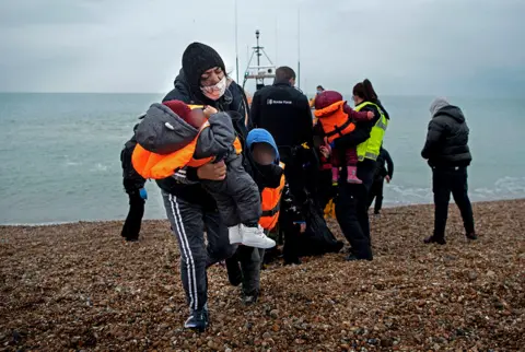 Ben Stansall / AFP A migrant carries her children (with faces blurred) after being helped ashore from a Royal National Lifeboat Institution lifeboat