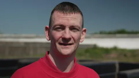 A close-up outdoor portrait of a man wearing a plain red sweatshirt.