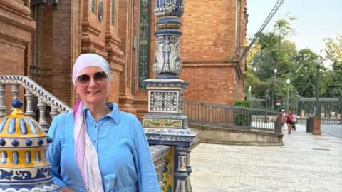 Natalia Zaman Natalia, a woman in a blue dress and a white and pink headscarf.