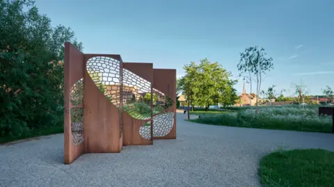 Michael Illas A brown sculpture which shows butterfly wings on a grey path