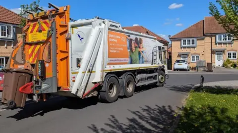 A large white rubbish truck stopped on a residential street. 