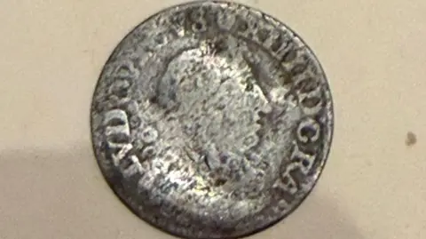 The coin is silver and has Roman numerals and a figurehead. The coin is slightly worn.