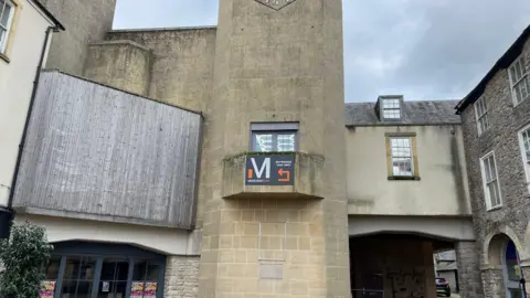 The Amulet theatre in Shepton Mallet. The building has a tower in the middle and a blue entrance door.