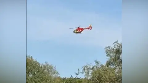 Sue Watkins A red air-ambulance helicopter flying in blue skies