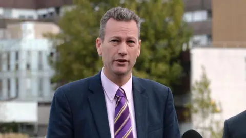 Getty image Nathan Gill, who has short, spici gray hair and is wearing a Navy suit with a lilac shirt and purple striped tie. 