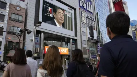 EPA People watch a television announcement on Abe's resignation