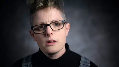 Rae in a BBC studio interview, wearing glasses and black top