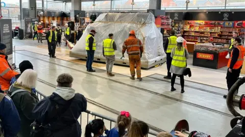 National Railway Museum People watch as the wrapped up Locomotive is pushed into the museum building on trolleys